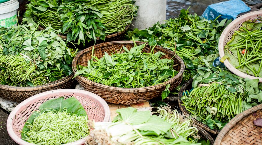 A variety of green herbs and vegetables in woven baskets laid out as if for a market